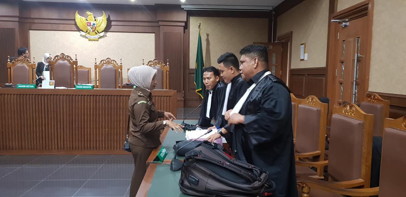 Bapak Raymond Simamora, S.H., M.H. (tengah) bersama tim penasihat hukumnya sedang berdiskusi dengan seorang petugas di ruang persidangan.