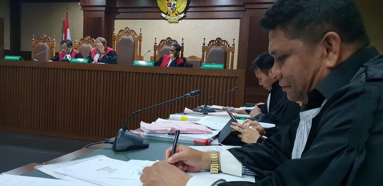 Suasana persidangan resmi di mana Raymond Simamora, S.H., M.H. (kanan) tampak sedang mencatat poin-poin penting di hadapan majelis hakim yang sedang memimpin jalannya sidang.