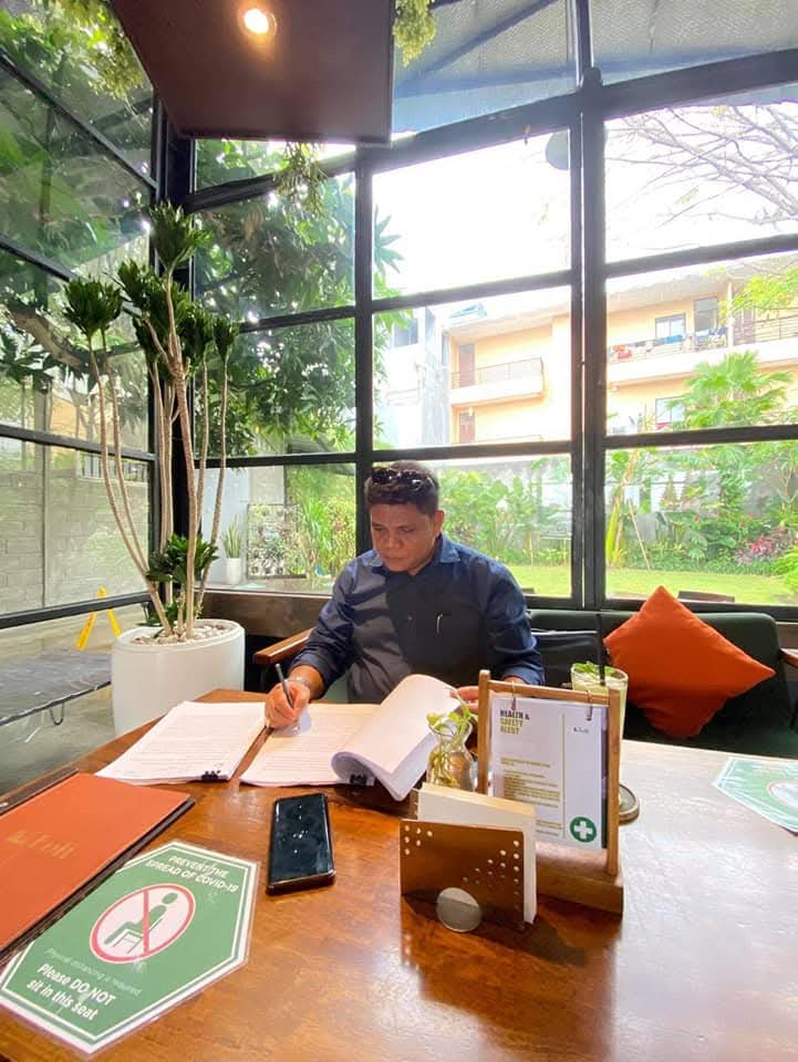 Potret Raymond Simamora, S.H., M.H. yang tampak fokus mencermati dan menandatangani dokumen hukum dalam suasana diskusi informal di sebuah kafe.